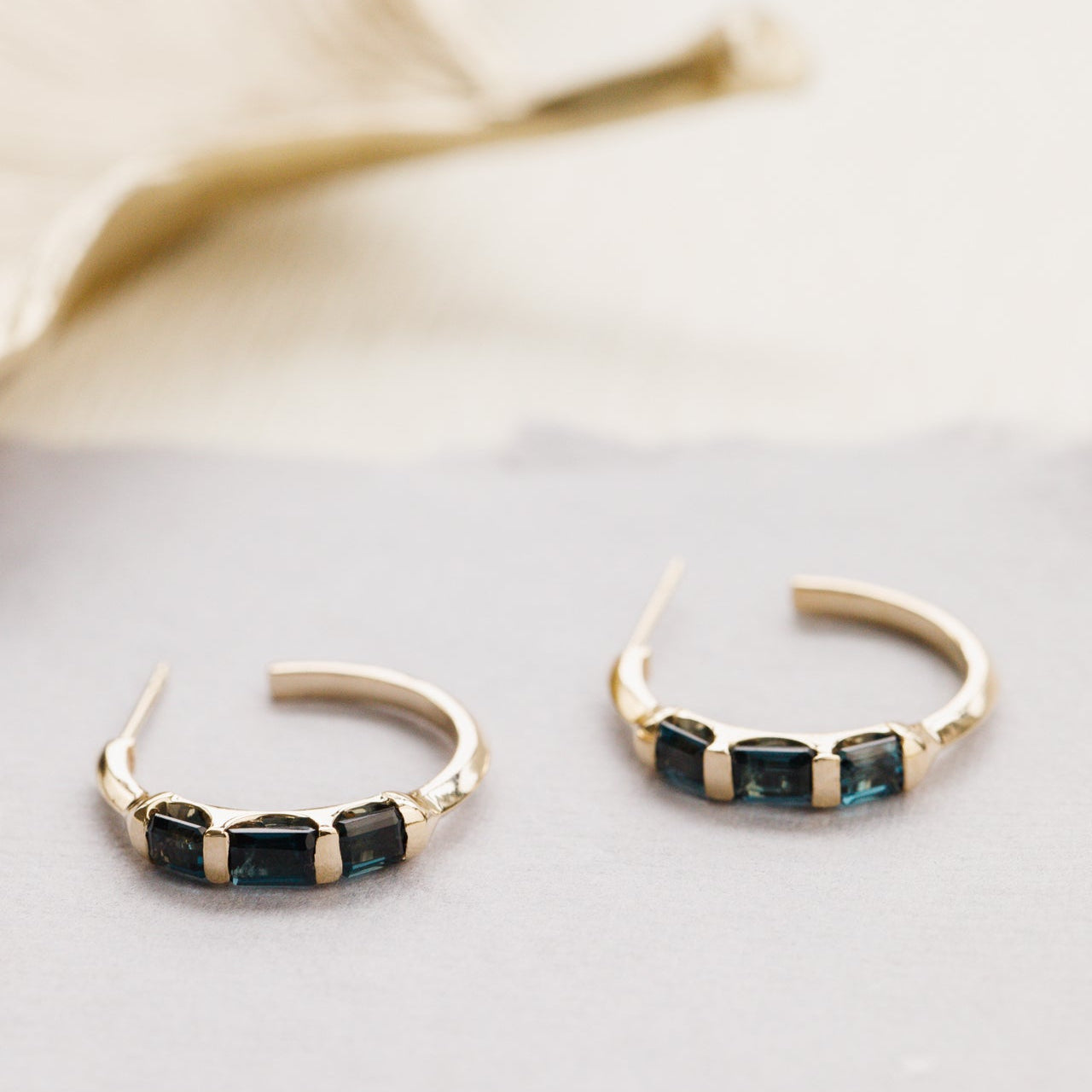 Gold hoop earrings with blue topaz gemstones on a light background
