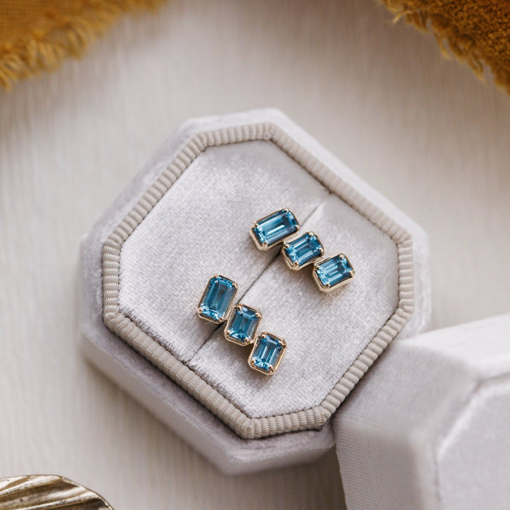 Pair of blue gemstone earrings in a hexagonal jewelry box on a textured surface.