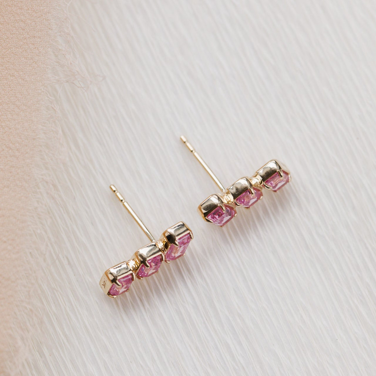 Gold earrings with pink gemstones on a light background