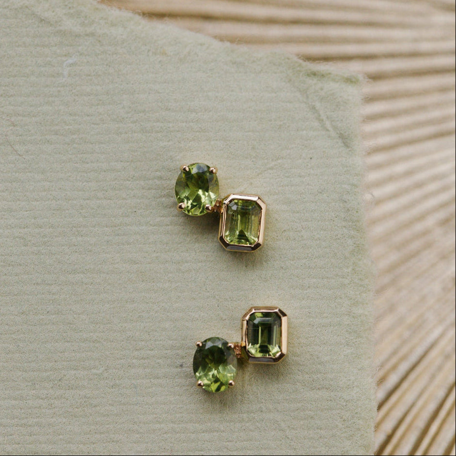 Pair of green gemstone earrings on a textured beige surface