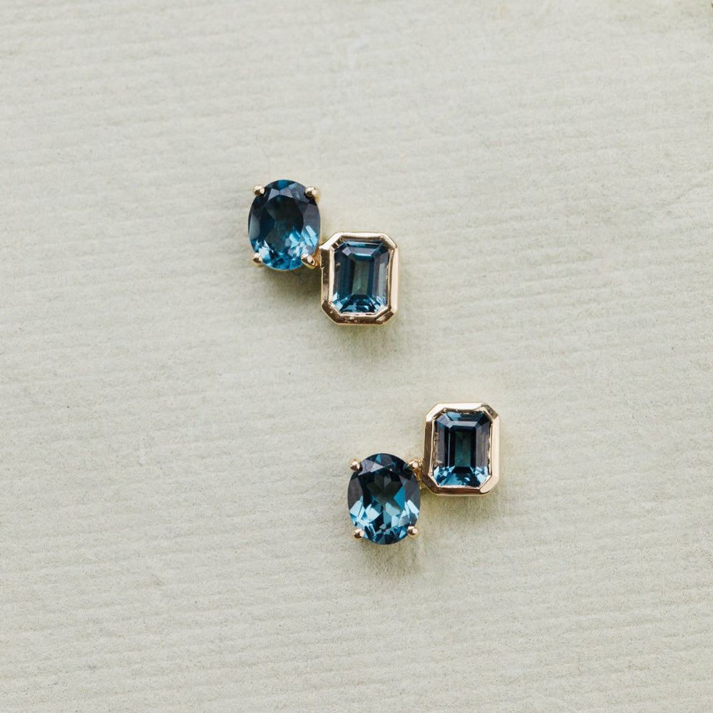 Pair of gold earrings with blue gemstones on a light gray background