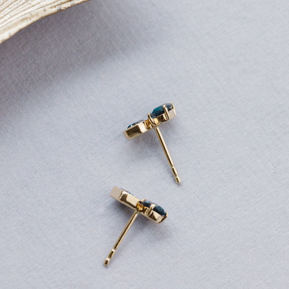 Gold earrings with blue gemstones on a light gray surface