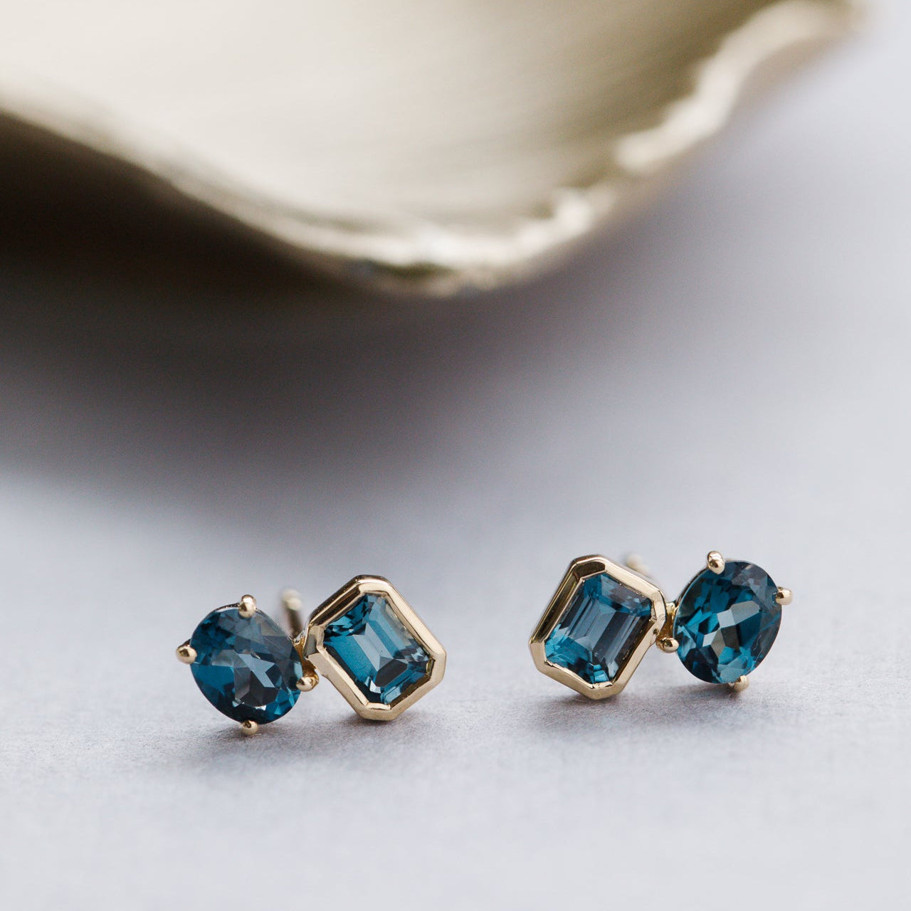 Pair of blue gemstone earrings with gold settings on a light background