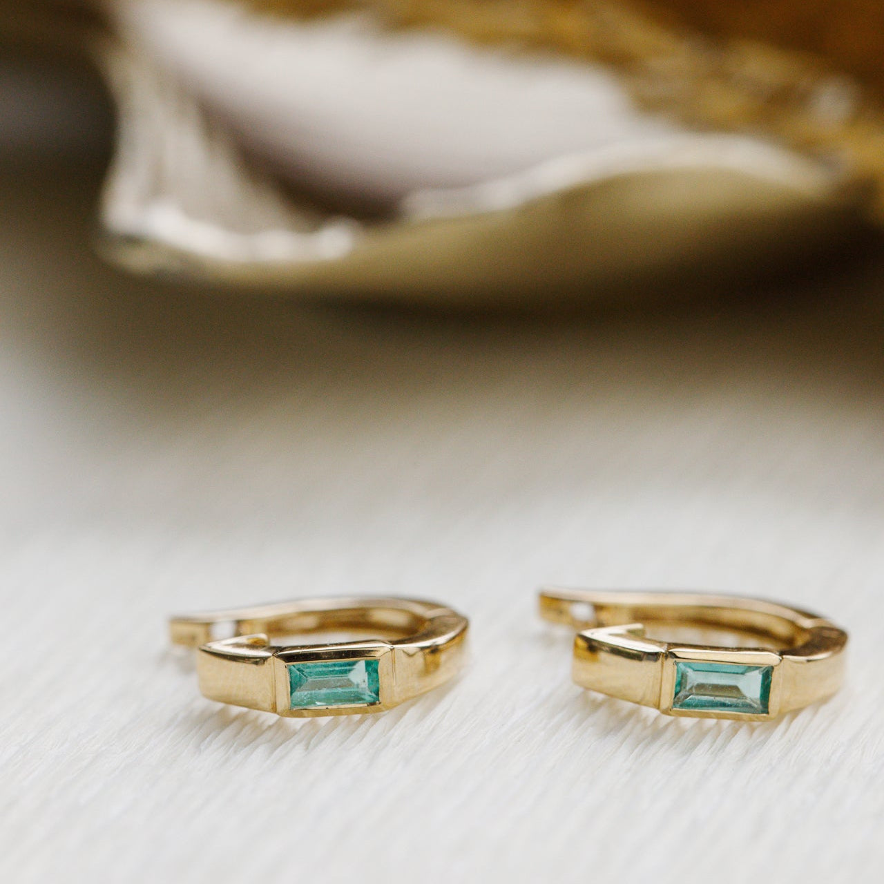 Gold rings with emerald green emerald gemstones on a textured surface