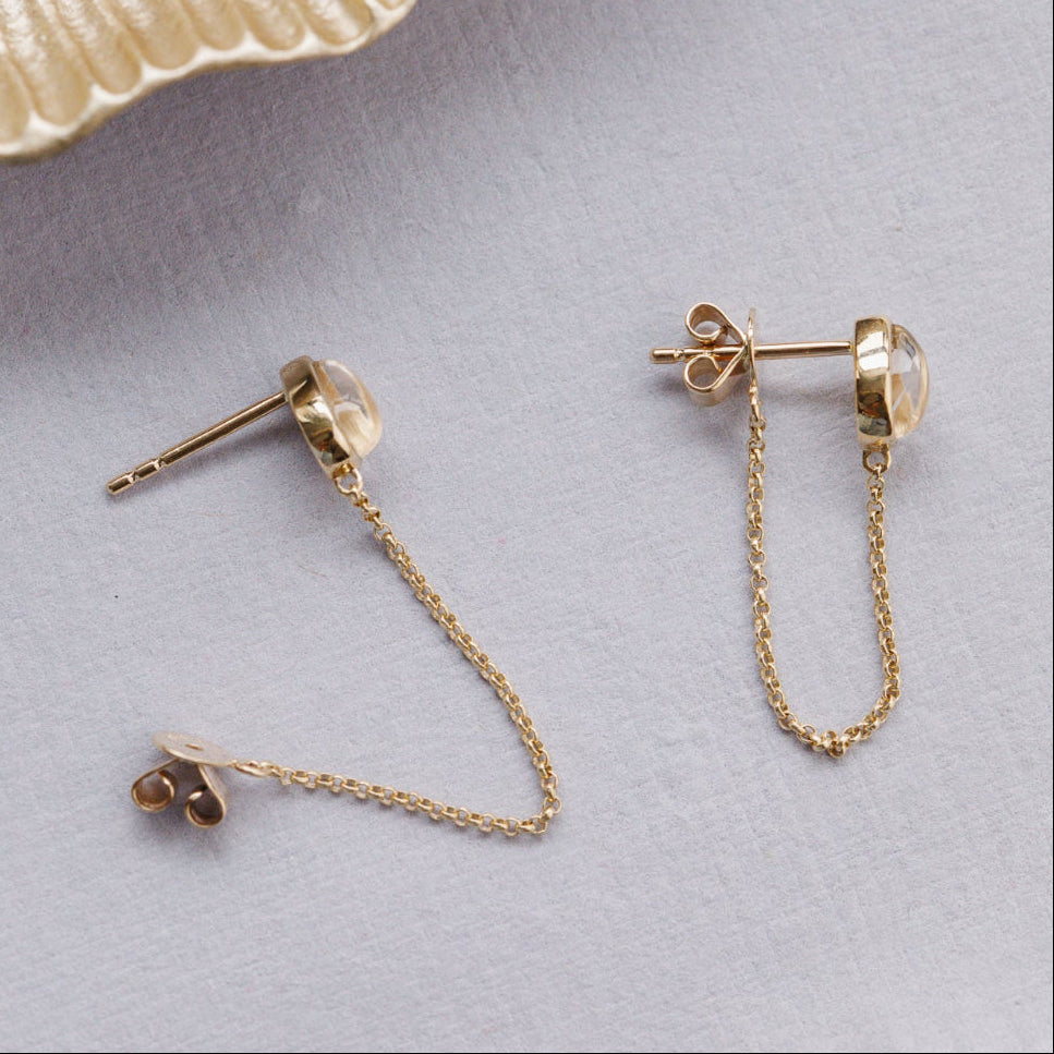 Gold chain earrings on a light gray surface.