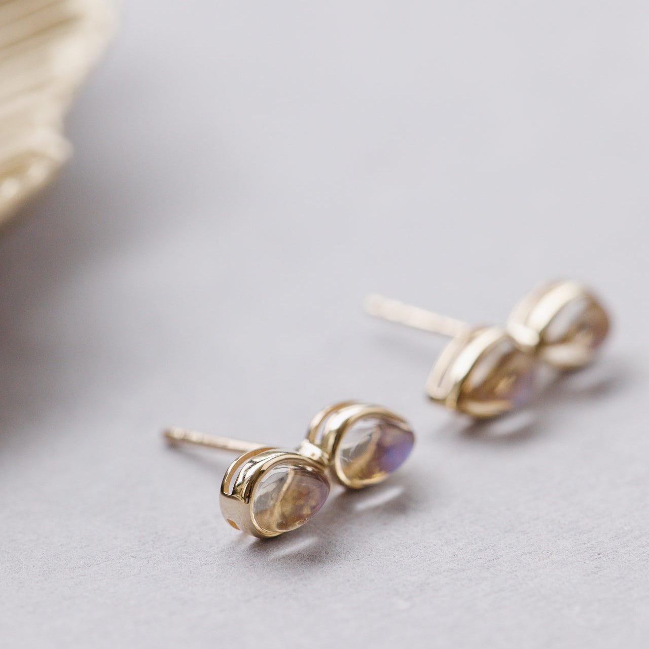Gold earrings with moonstone gemstones on a light gray surface