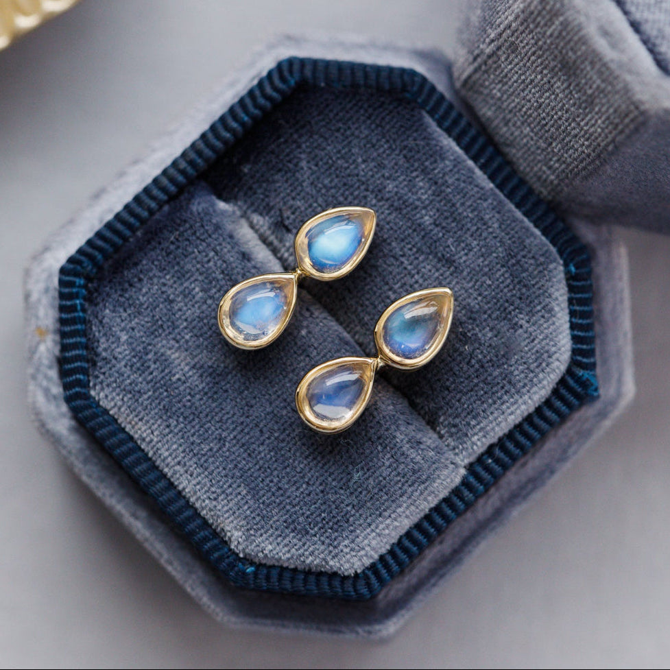 Pair of gold earrings with blue gemstones on a hexagonal blue velvet cushion.