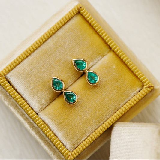 Pair of emerald green pear earrings on a yellow velvet cushion
