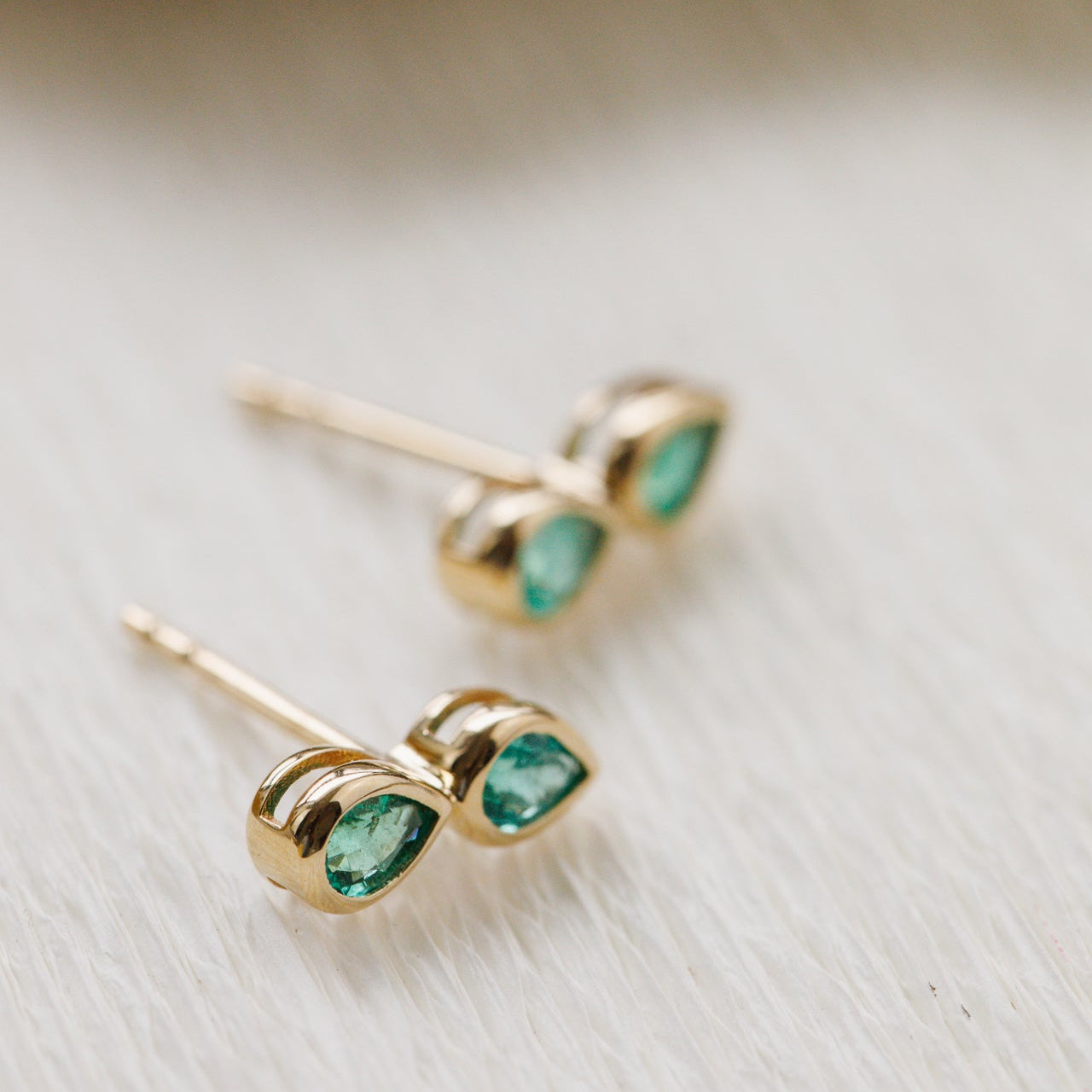 Gold earrings with green gemstones on a light wooden surface