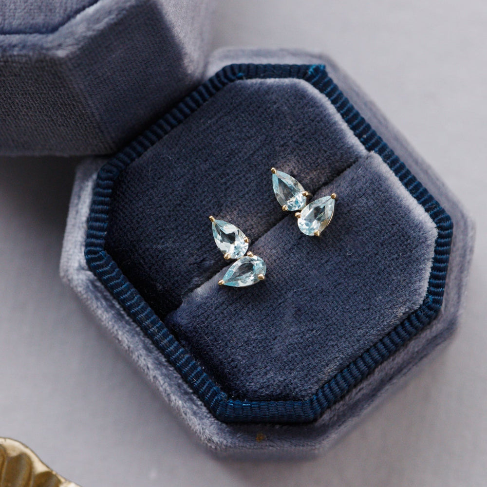 Pair of blue topaz earrings in a blue jewelry box on a light gray surface