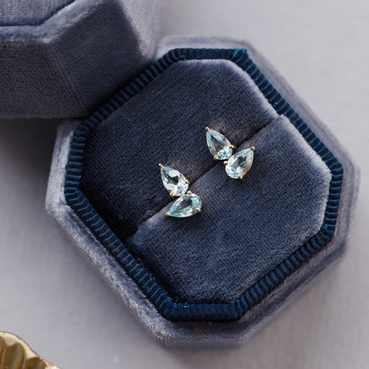 Pair of blue topaz earrings in a blue jewelry box on a light gray surface