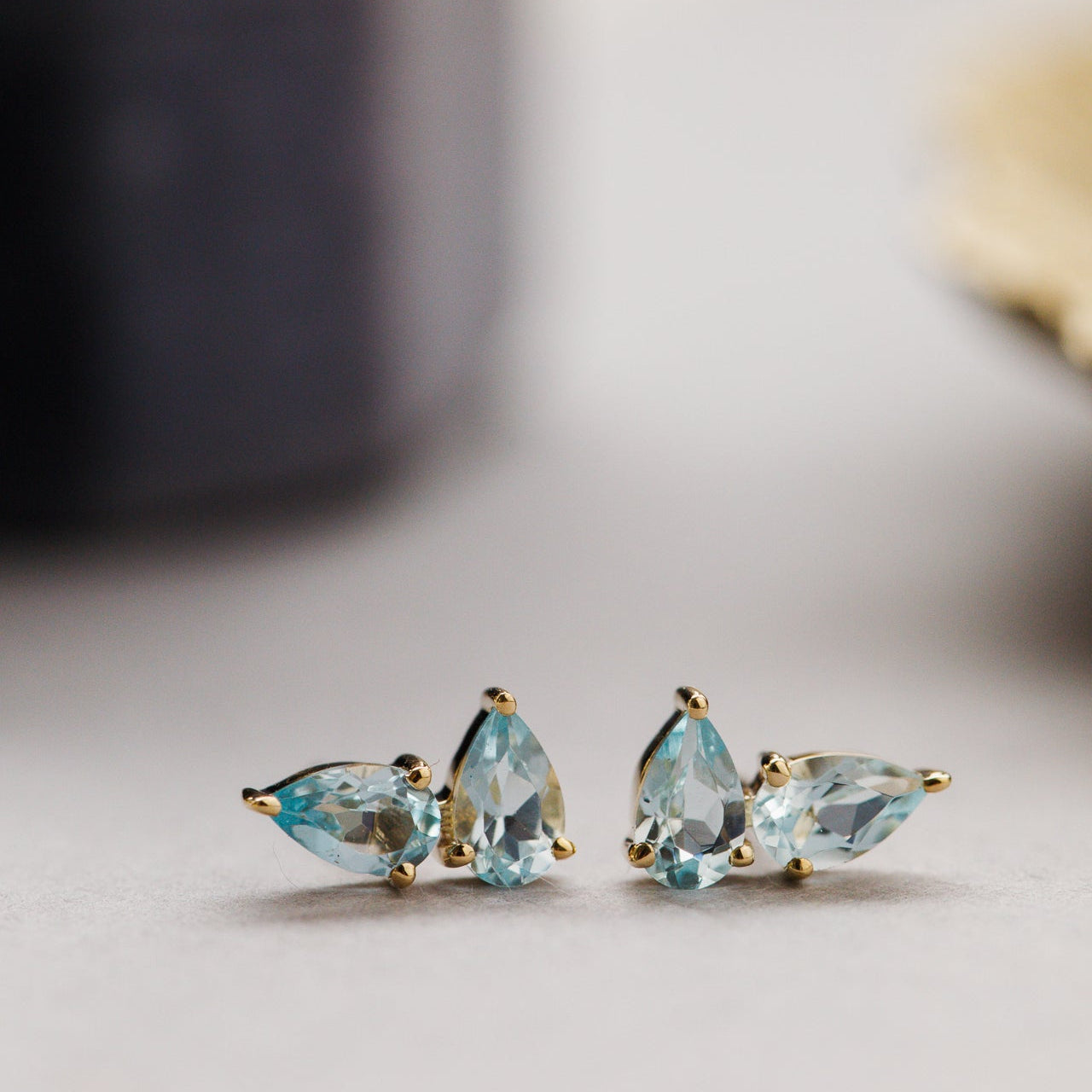 Pair of gold and blue topaz pear earrings on a neutral background