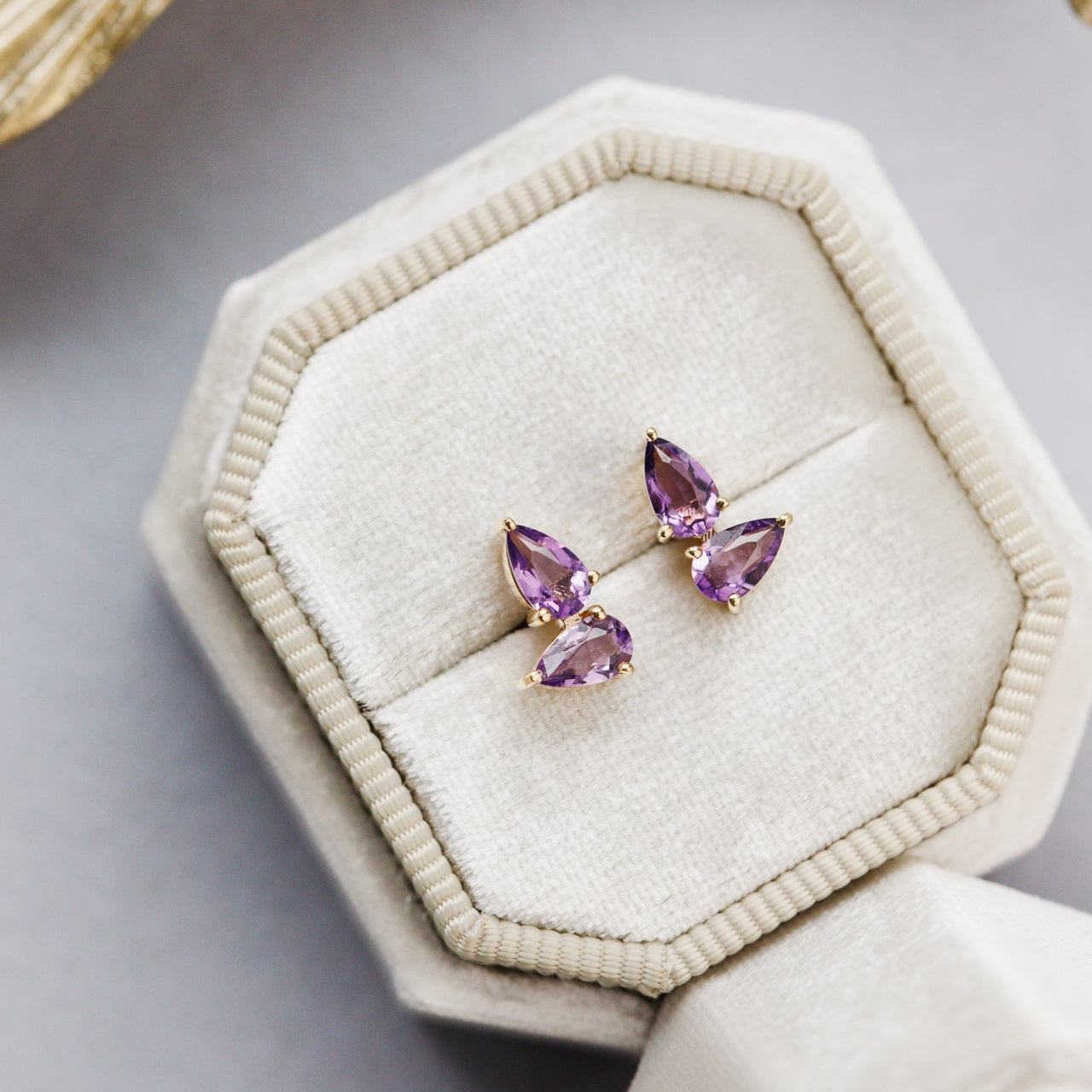 Pair of purple gemstone earrings on a beige jewelry display box.