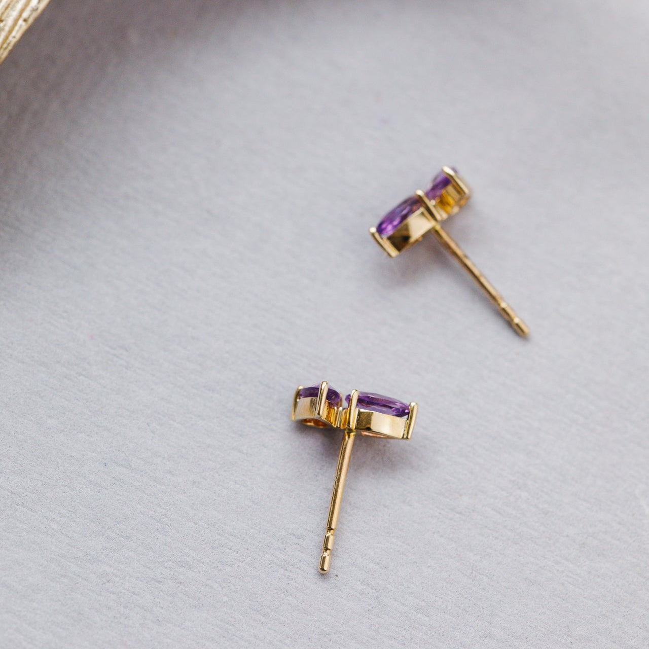 Gold earrings with purple gemstones on a light gray background