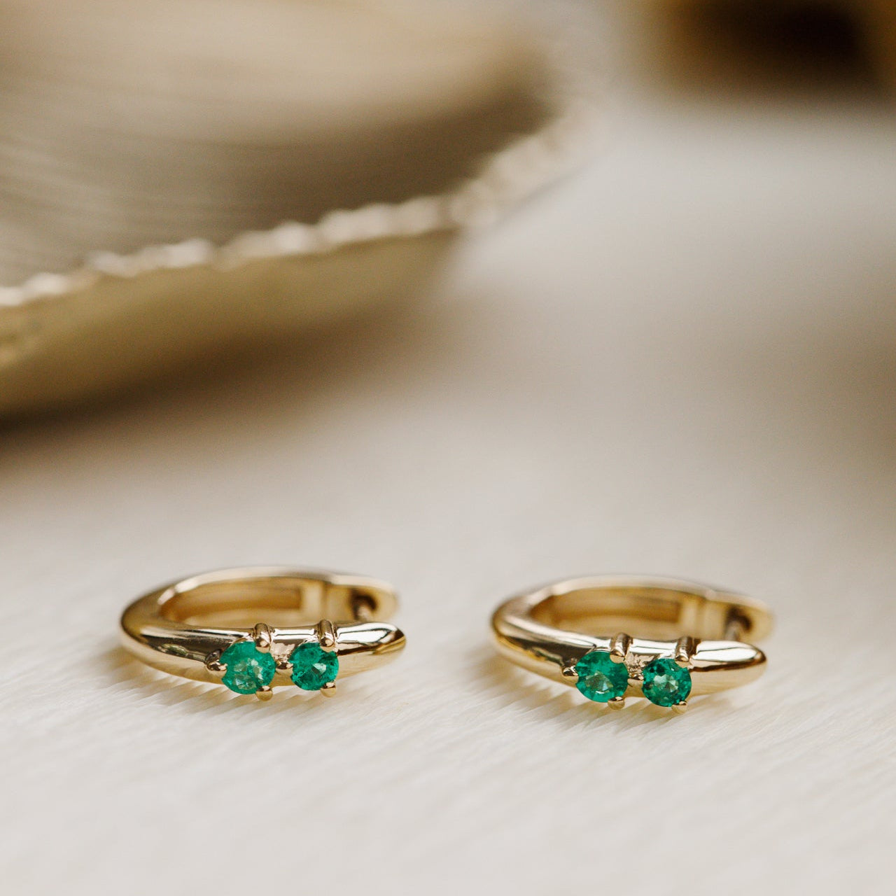 Pair of gold rings with emerald stones on a light background