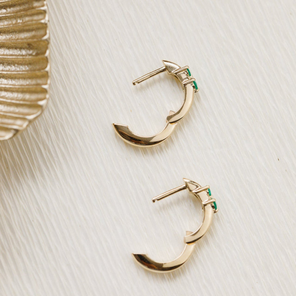 Gold hoop earrings with green gemstones on a textured white surface