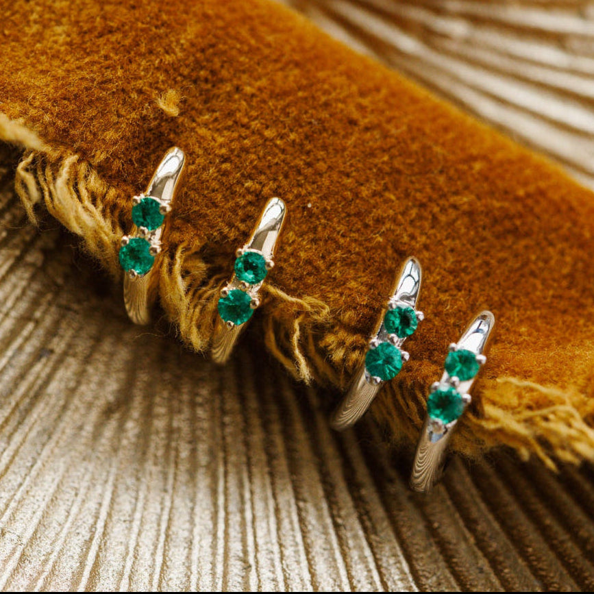 Gold rings with green gemstones on a textured surface