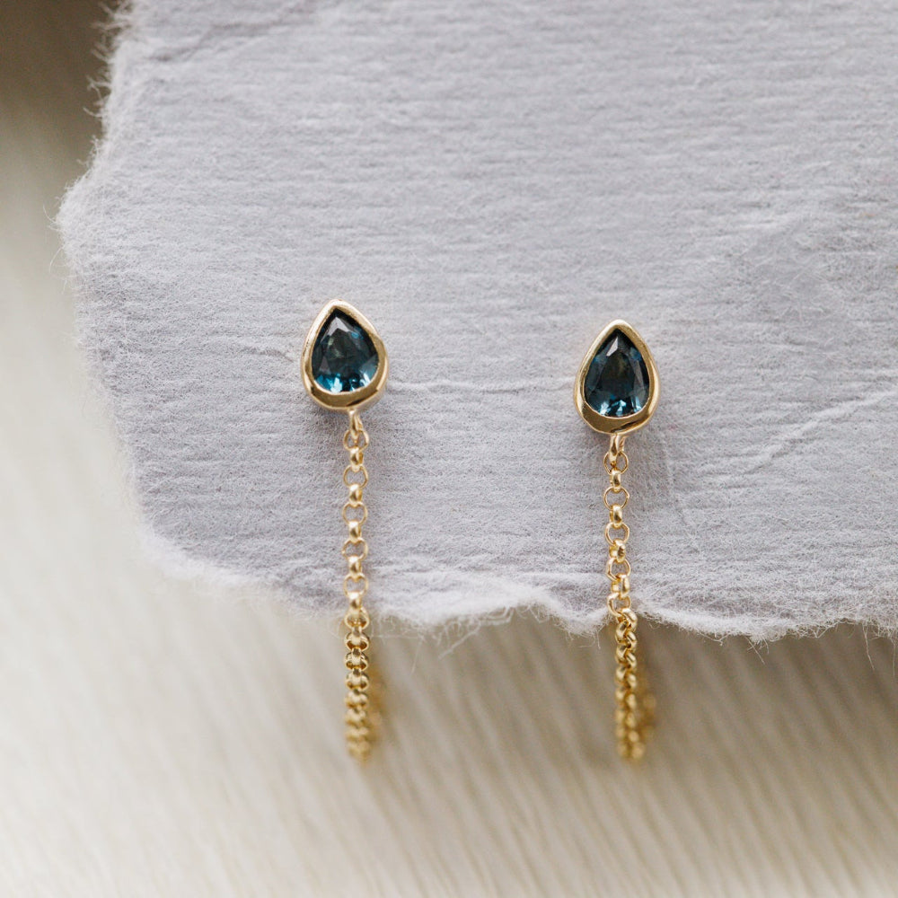 Gold earrings with London blue topaz gemstones on a soft fabric background