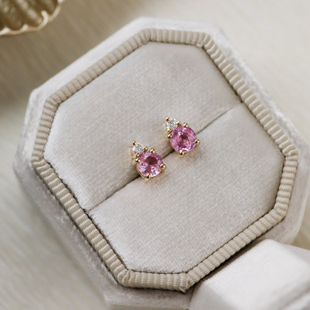 Pink sapphire gemstone earrings on a beige jewelry cushion