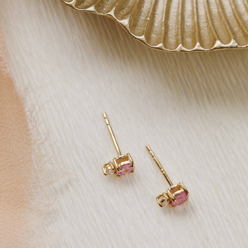 Gold earrings with pink sapphire gemstones on a light wooden surface