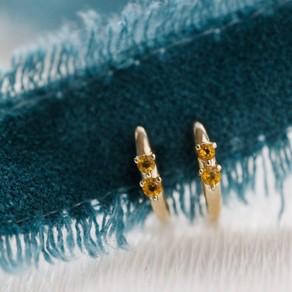 Gold earrings with yellow gemstones on a textured blue fabric background