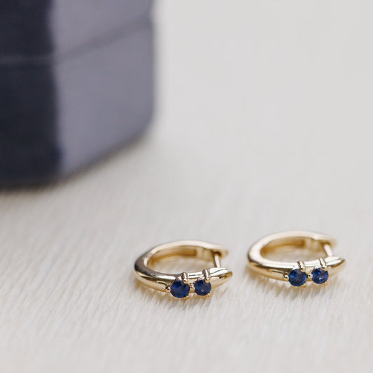 Gold hoop earrings with blue gemstones on a light gray surface.