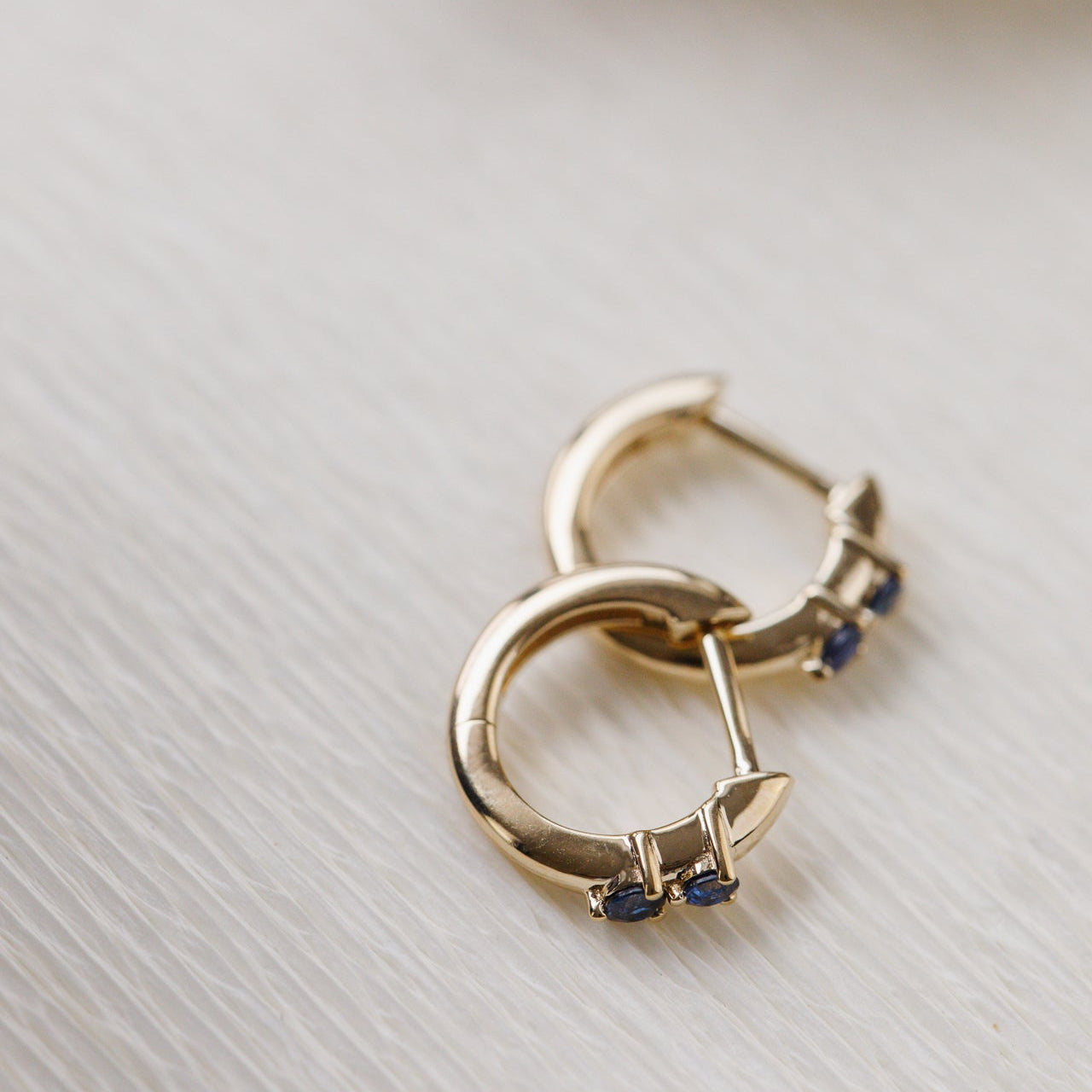 Gold hoop earrings with blue gemstones on a light background