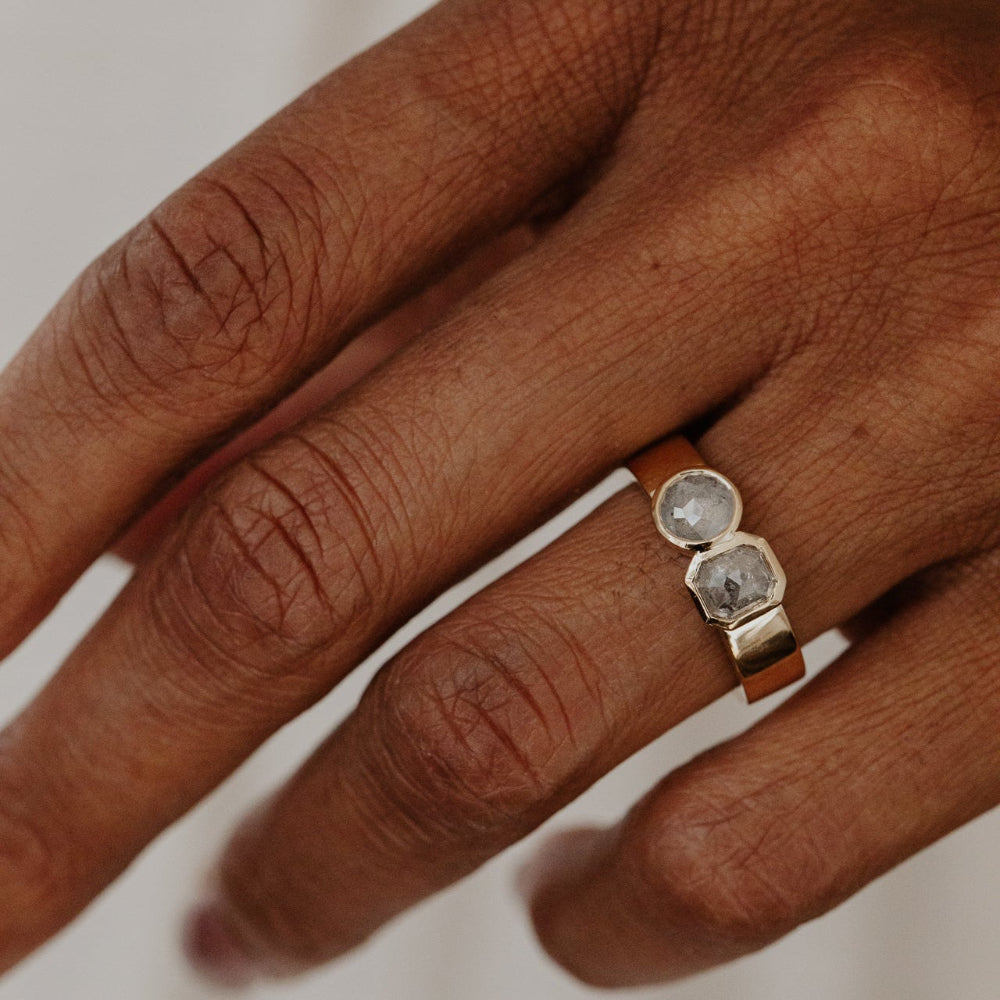 Hand wearing a Madison ring with two clear rustic diamond stones on a neutral background.