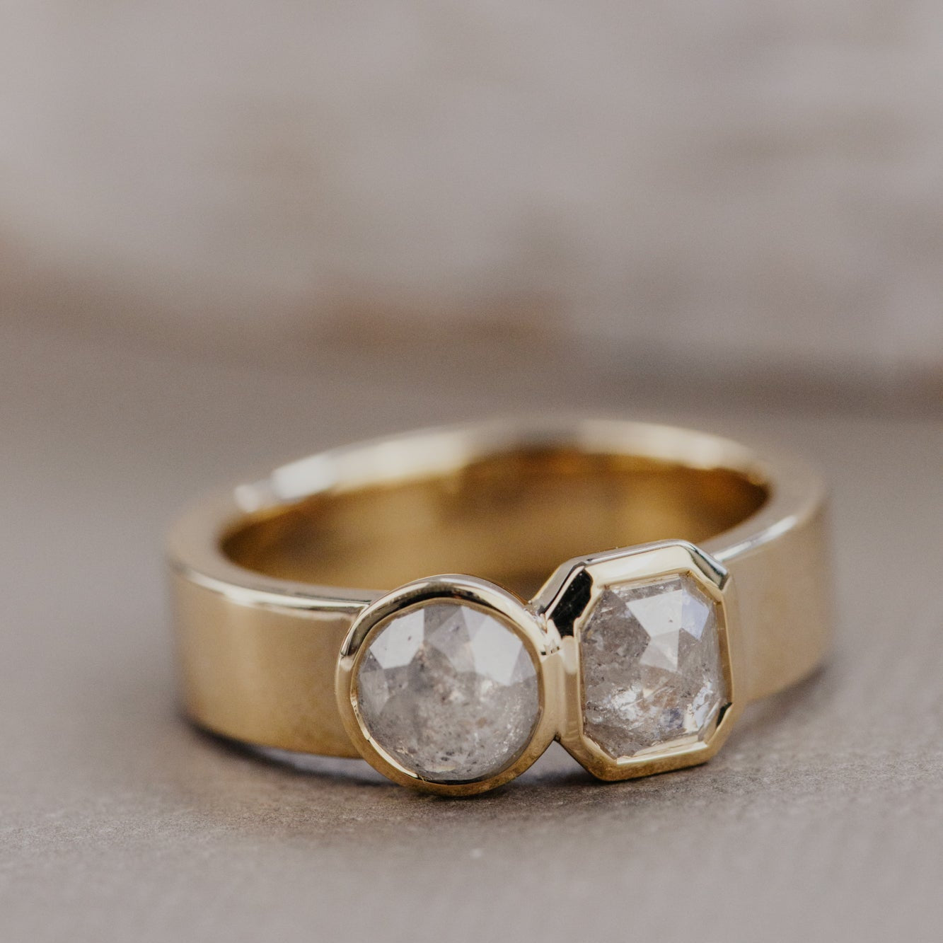 Gold ring with two rustic diamonds on a neutral background.