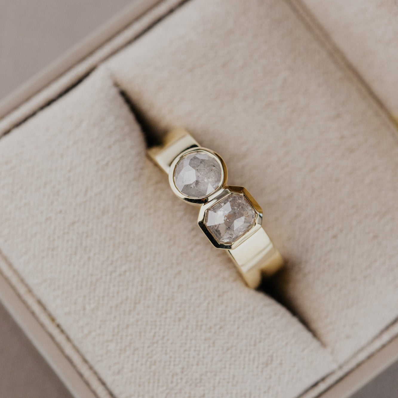 Gold ring with two rustic diamonds on a beige cushioned box.