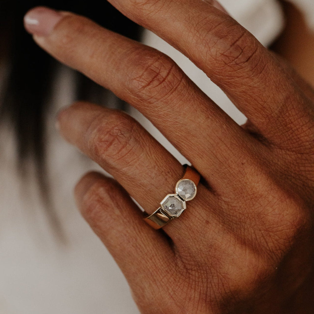 Close-up of a hand wearing a gold ring Madison with two rustic diamond stones against a blurred background.