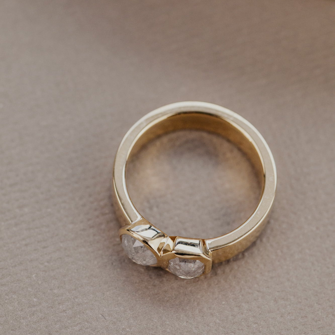 Gold ring with rustic diamond stones on a beige surface.