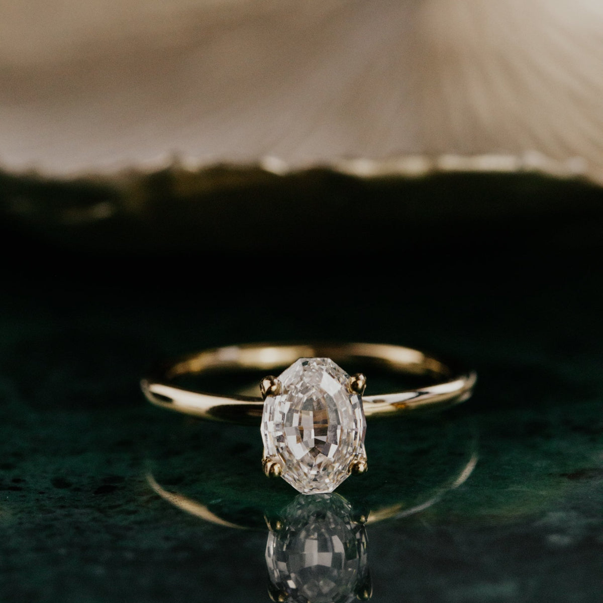 Gold ring with a oval diamond on a reflective surface.