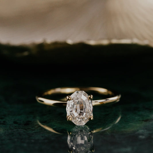 Gold ring with a oval diamond on a reflective surface.