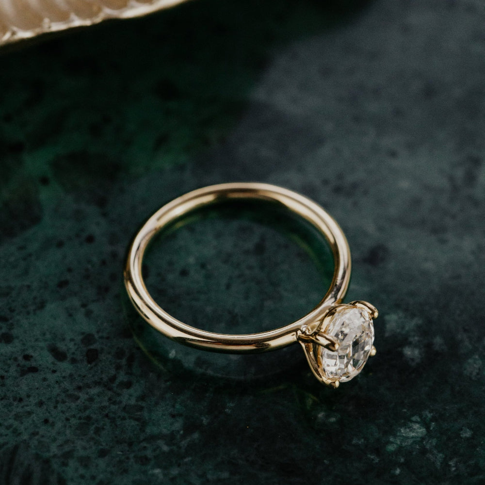 Gold ring with a diamond on a dark textured surface.