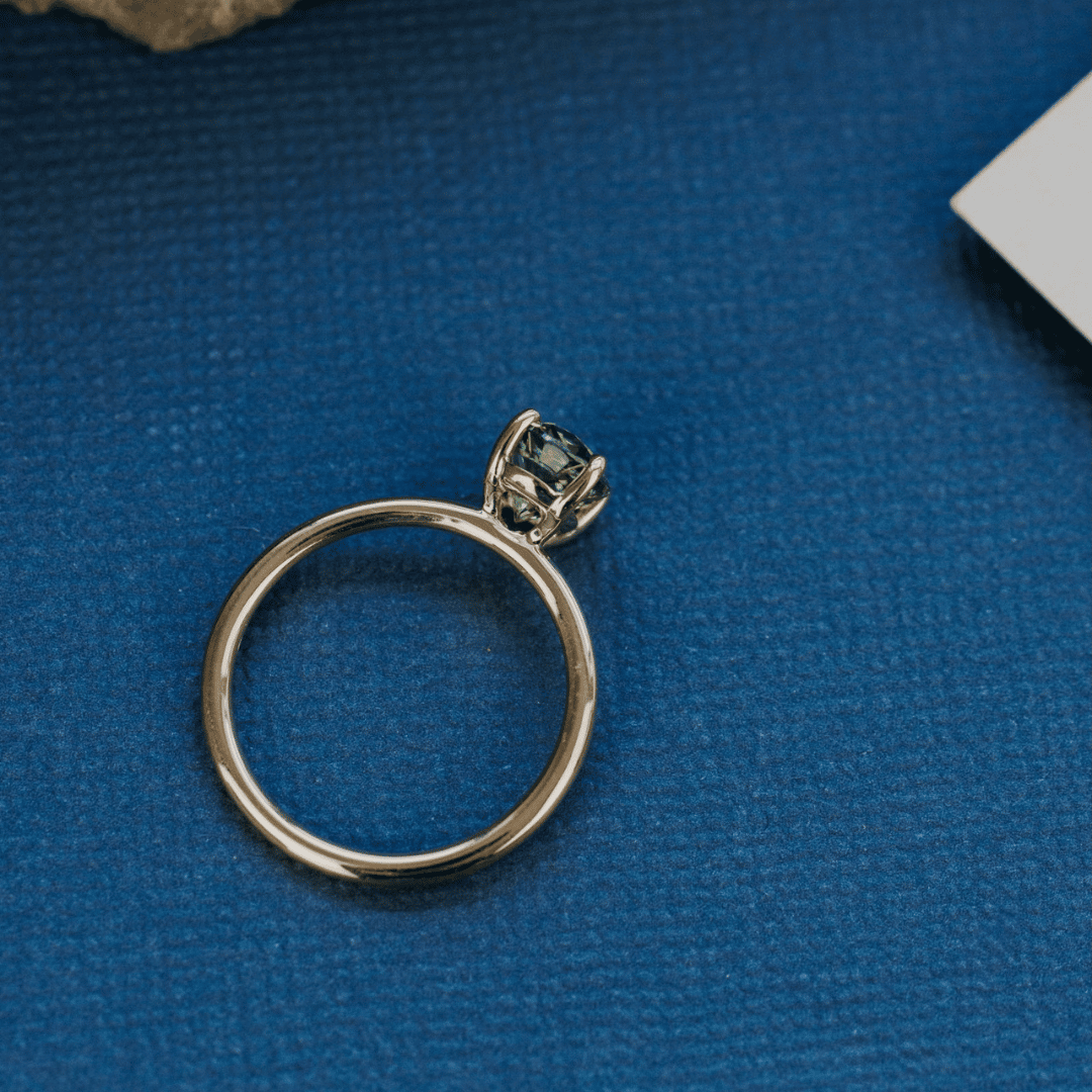 A 14k gold ring featuring a blue sapphire gemstone, displayed on a textured blue surface from a top view.
