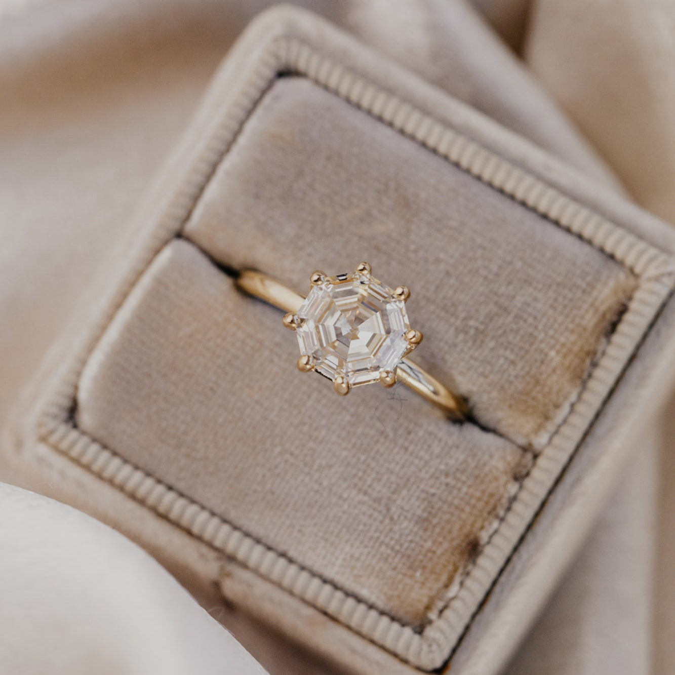Champagne diamond ring in a beige velvet box on a soft beige background.