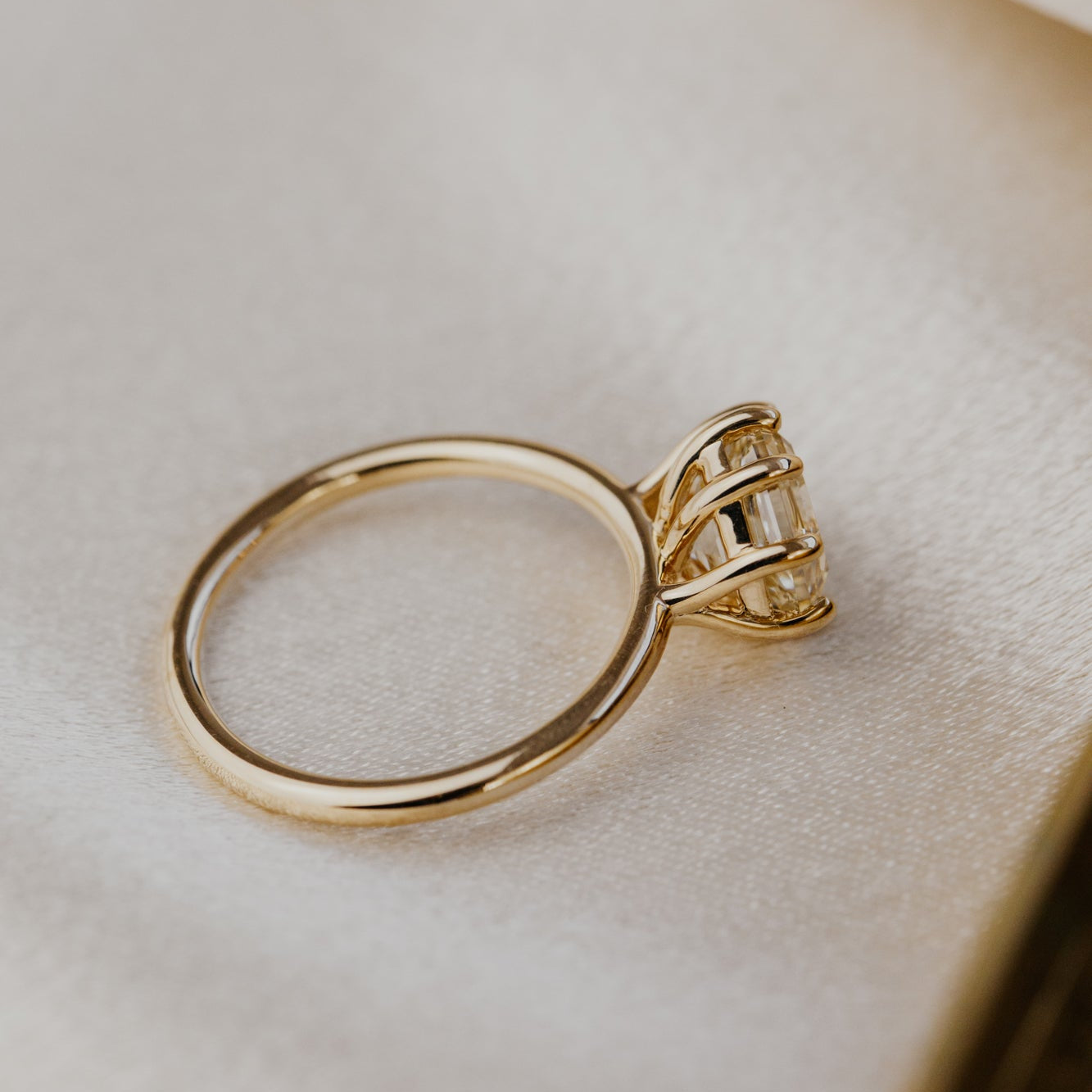 Gold ring with a diamond on a soft beige background.