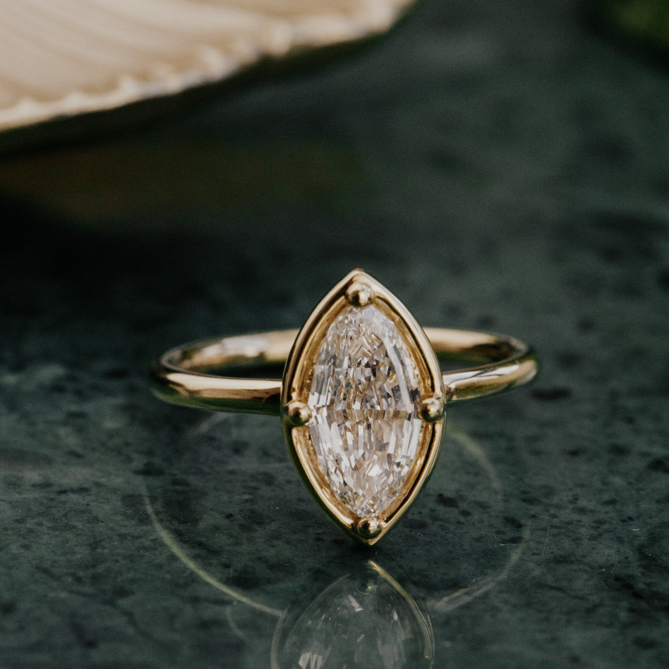 Gold ring with a marquise lab grown diamond on a dark surface.