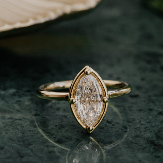 Gold ring with a marquise lab grown diamond on a dark surface.