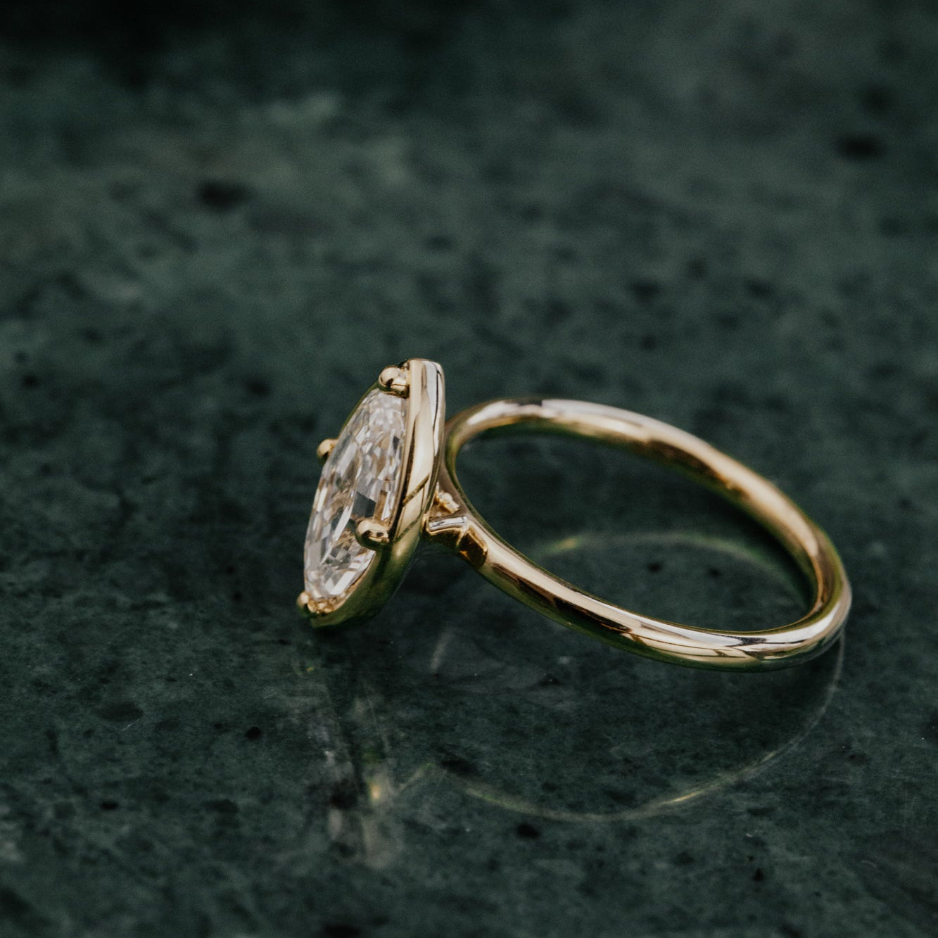 Gold ring with a marquise lab grown diamond on a dark textured surface.