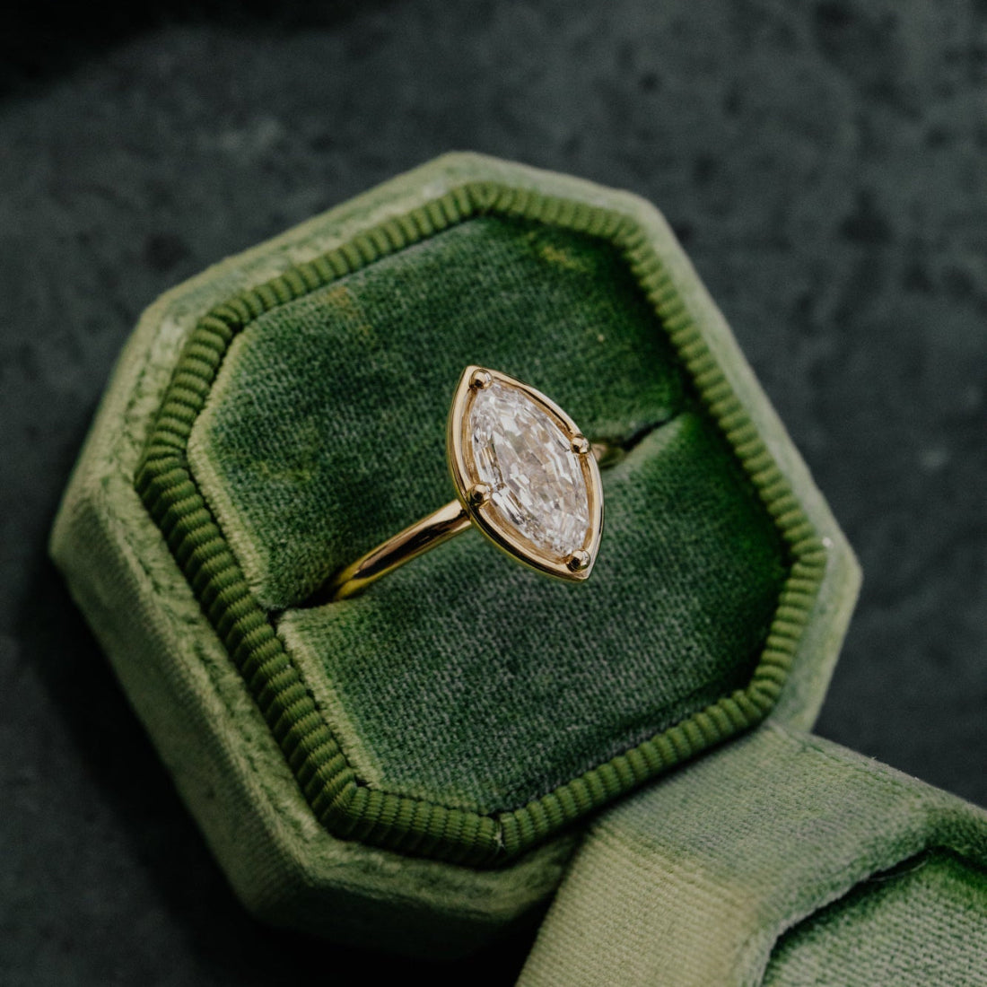 Marquise lab grown diamond ring in a green velvet box on a dark textured surface.