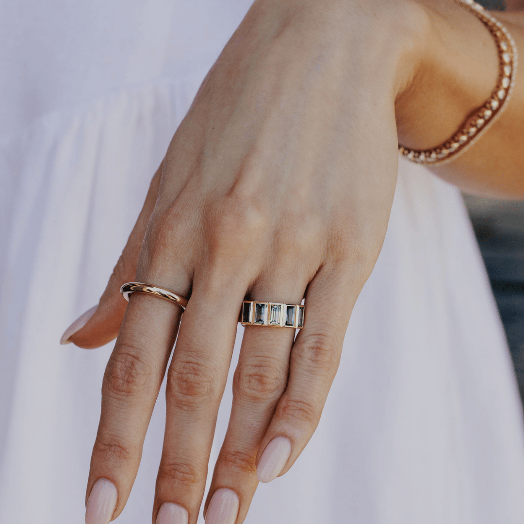 A 14k gold ring featuring multiple blue baguette-shaped sapphire gemstones, displayed on the ring finger of a hand model with a soft-focus background.