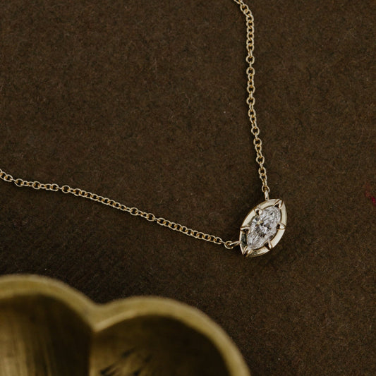 Gold necklace with a diamond pendant on a brown textured background.