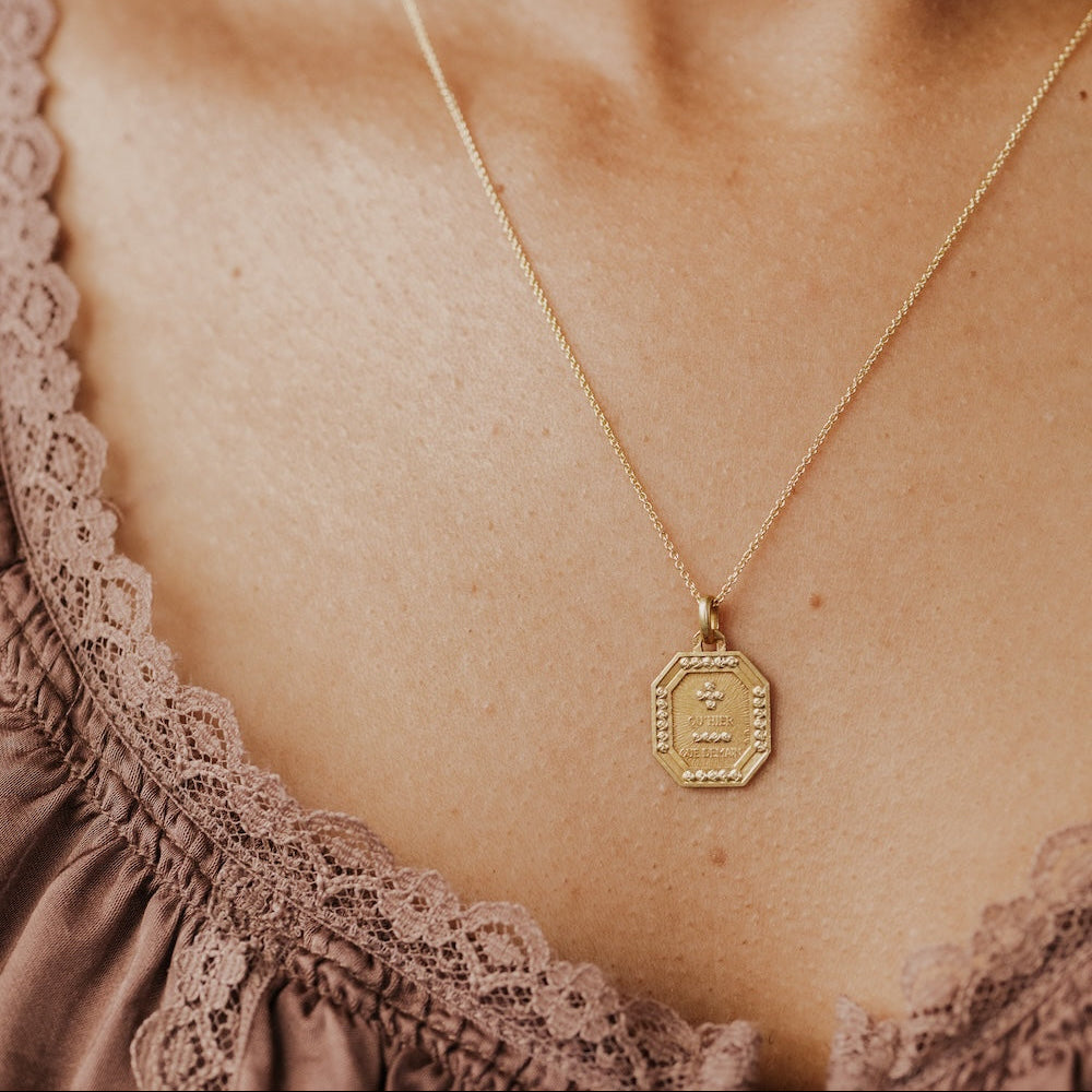 The Medium Rectangular 18k Yellow Gold Vintage Love Token with Rose Border by A. Augis, an octagonal 18k yellow gold vintage pendant with a rose-motif border and the engraved phrase "qu'hier que demain," worn on a delicate gold chain against a model's chest.