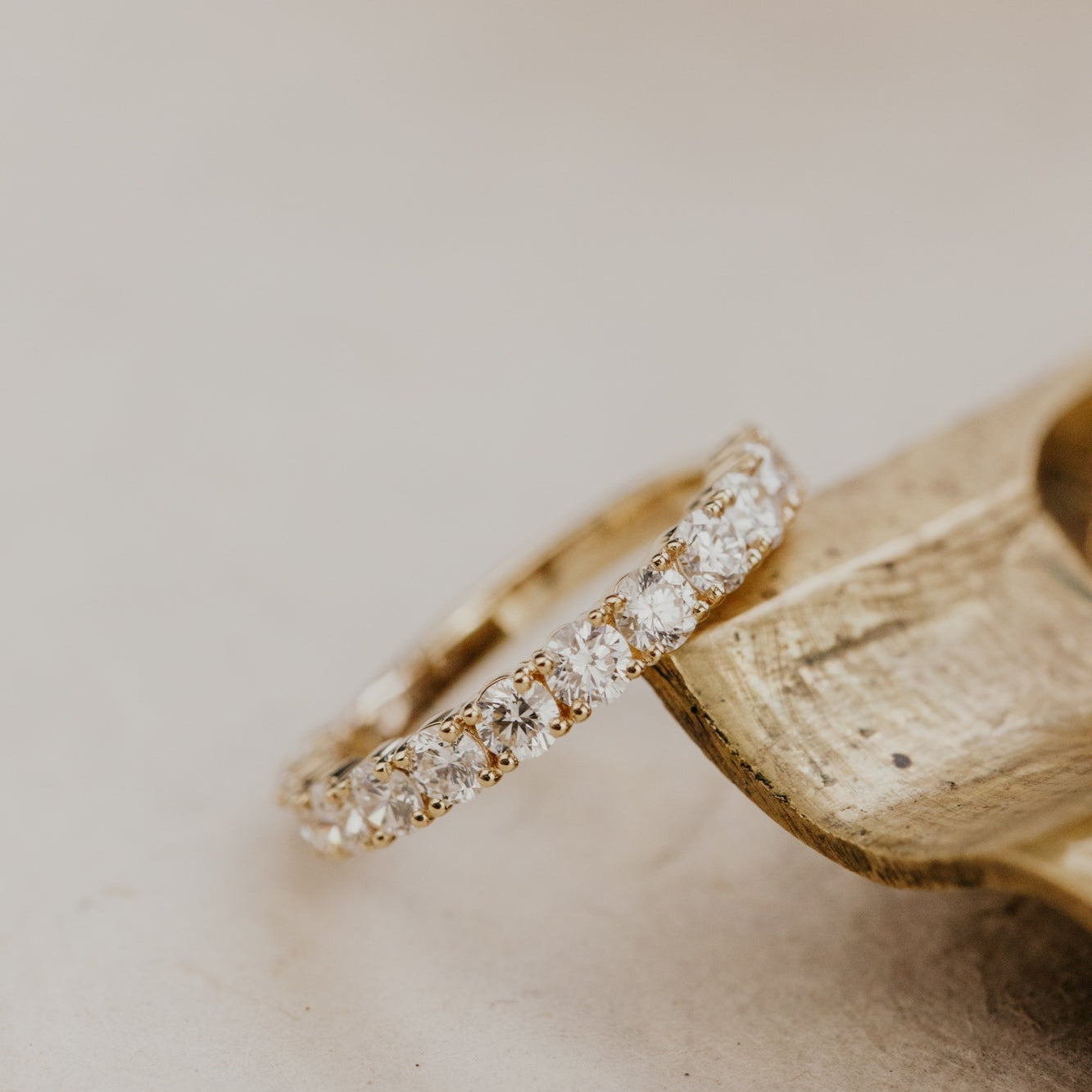 The mini Amara round diamond wedding band placed on a wood surface with a white background.