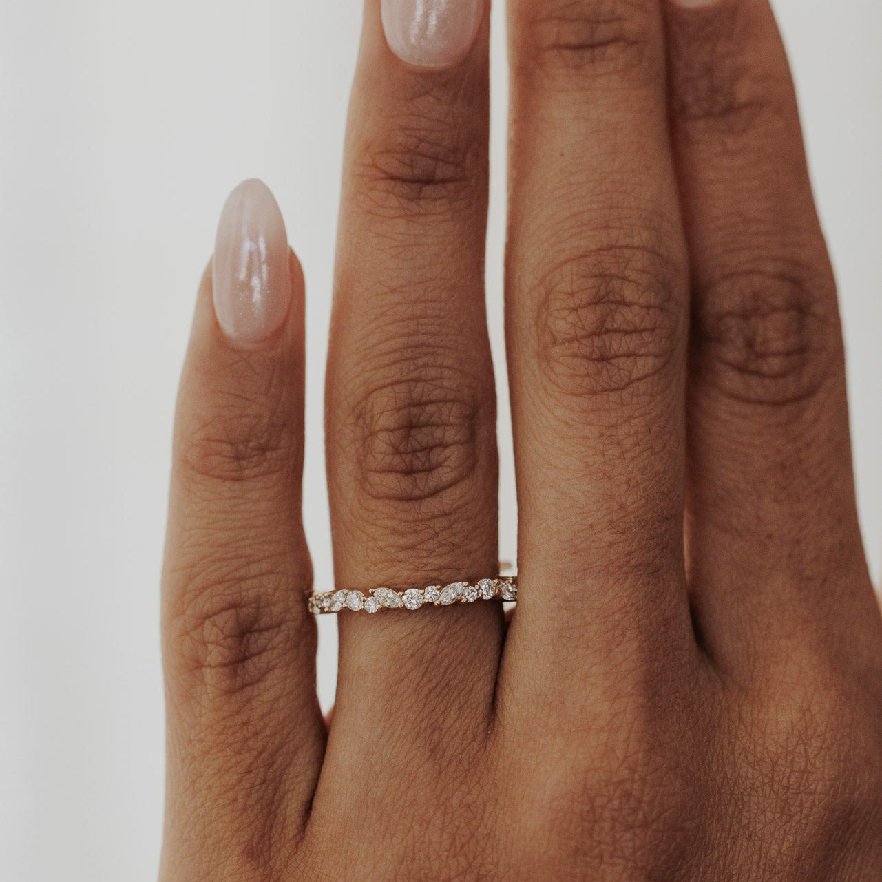 Hand wearing a Mini Natalie wedding band with diamonds on a plain background.