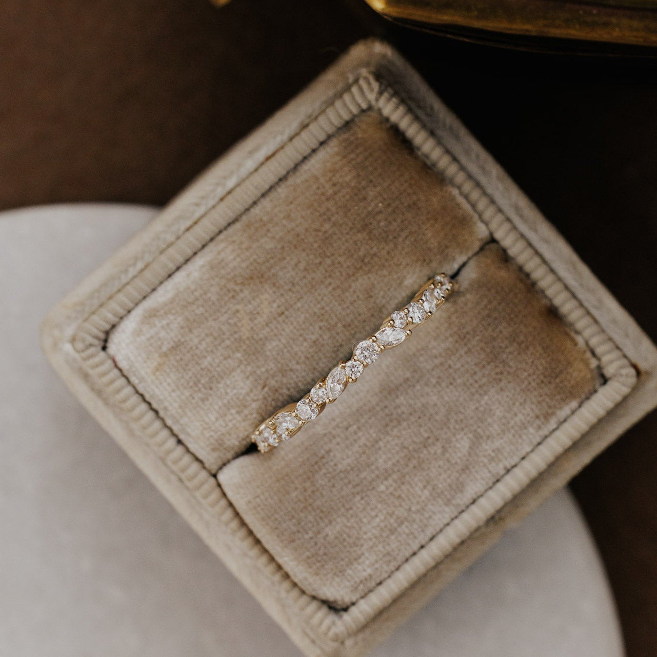 Mini Natalie Diamond wedding band in a beige jewelry box on a soft surface.