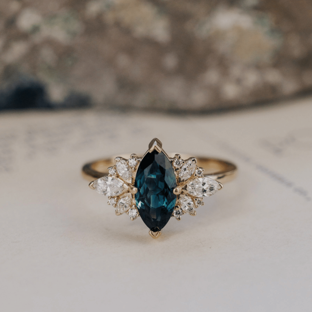 A 14k gold ring featuring a blue sapphire gemstone viewed from straight on, displayed on a textured white surface.
