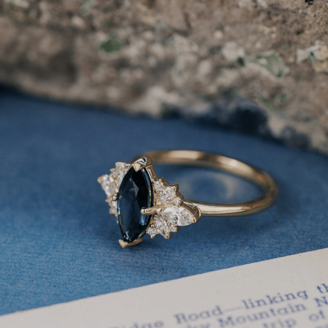 A 14k gold ring featuring a blue sapphire gemstone viewed from an angle, displayed on a textured blue surface.